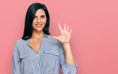 Gündelik giysiler giyen genç beyaz kadın beş numarayı gösterip işaret ederken kendinden emin ve mutlu gülümsüyor.. 