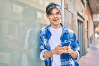 Genç İspanyol adam şehirde akıllı telefon kullanarak mutlu gülümsüyor..