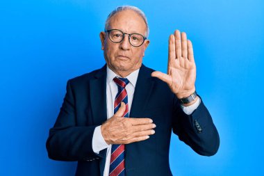 Beyaz üst düzey bir adam, iş elbisesi ve kravat takmış, avucunda ve göğsünde yeminle yemin ediyor. 