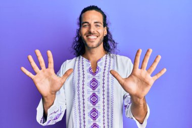 Uzun saçlı, bohem ve hippi tişörtlü genç ve yakışıklı bir adam on numaralı parmaklarıyla kendini beğenmiş ve mutlu gülümserken kendini gösteriyor.. 