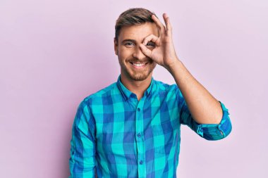 Yakışıklı, beyaz bir adam, günlük kıyafetler giyiyor, gülümsüyor, gülümsüyor. Elleri gözlerinde, parmaklarının arasından bakıyor. 