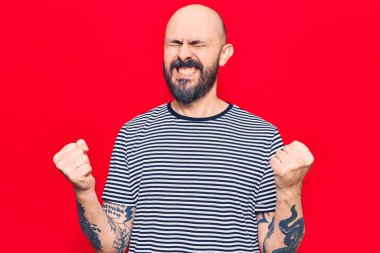 Gündelik kıyafetler giyen, mutlu ve heyecanlı genç bir adam kollarını kaldırmış, gülümseyen ve başarı için çığlık atan kazanan bir jest yapıyor. kutlama konsepti. 