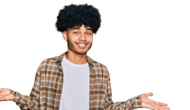 Afro saçlı, sıradan kıyafetler giyen, elleri ve kolları havada, kafası karışmış genç Afrikalı Amerikalı bir adam. şüphe kavramı. 