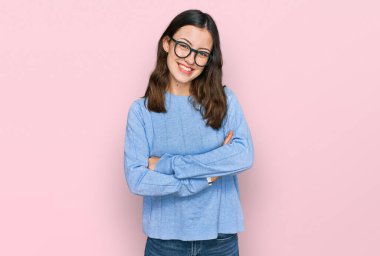 Sıradan kıyafetler ve gözlük takan, kollarını kavuşturup kameraya gülümseyen genç ve güzel bir kadın. pozitif kişi. 