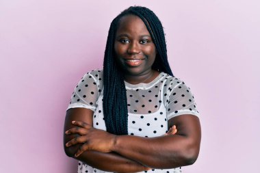 Saçları örgülü, mutlu yüzlü, kolları çaprazlanmış, kameraya bakan genç siyahi bir kadın. pozitif kişi. 