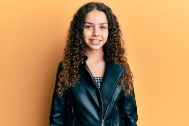 Siyah deri ceket giyen genç İspanyol kız pozitif ve mutlu görünüyor ve kendine güvenen bir gülümsemeyle dişlerini gösteriyor. 
