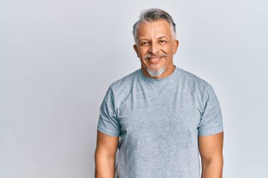 Orta yaşlı, gri saçlı, sıradan kıyafetler giyen, yüzünde mutlu ve havalı bir gülümseme olan bir adam. şanslı kişi. 