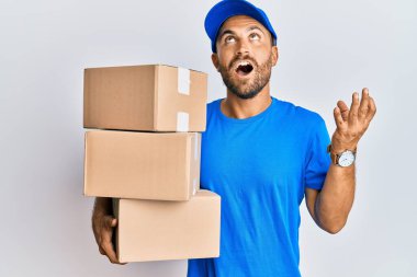 Sakallı, kurye üniforması giyen yakışıklı adam teslimat paketleri taşıyor. Deli gibi bağırıyor, bağırıyor, agresif bir ifade ve kollarıyla bağırıyor. hüsran kavramı. 