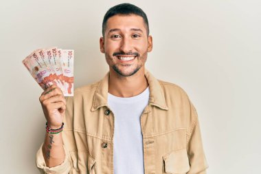 Elinde 10 Kolombiya pezosu olan yakışıklı bir adam. Olumlu ve mutlu görünüyor. Kendine güvenen bir gülümsemeyle dişlerini gösteriyor. 