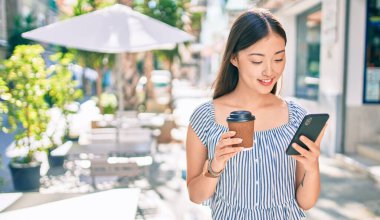 Genç Çinli kadın akıllı telefon kullanıyor. İçki içiyor. Şehir caddesinde kahve içiyor..