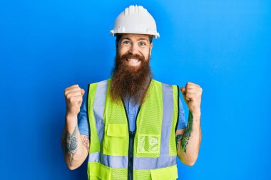 Uzun sakallı, güvenlik kaskı takan ve yansıtıcı ceketli kızıl saçlı adam kollarını kaldırıp, gözlerini açarak başarıyı kutluyor ve şaşırıyor. Kazanan konsept. 