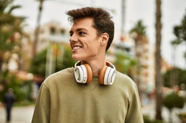 Şehirde kulaklık takarak mutlu gülümseyen genç İspanyol adam..