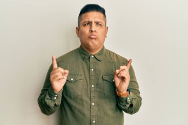 Gündelik kıyafetler giyen genç latin adam üzgün ve üzgün görünüyor, parmaklarıyla yön gösteriyor, mutsuz ve depresif.. 