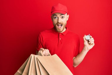 Elinde teslimat çantaları ve geri sayım saati olan genç kızıl saçlı adam çılgın ve şaşırmış bir şekilde başarıyı kutluyor.. 