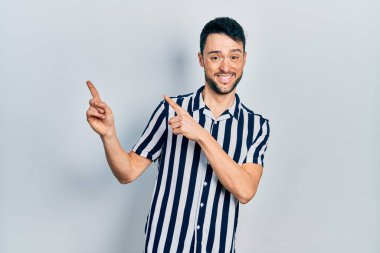 Gündelik kıyafetler giyen genç İspanyol adam gülümseyip kameraya bakıyor ve iki eliyle ve parmaklarıyla kenarı işaret ediyor.. 