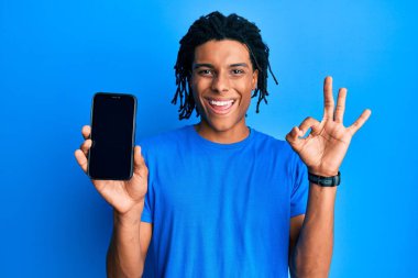 Genç Afro-Amerikan adam elinde akıllı telefonuyla ekranda boş görünüyor. Tamam işareti yapıyor, gülümsüyor ve mükemmel bir sembol oluşturuyor. 