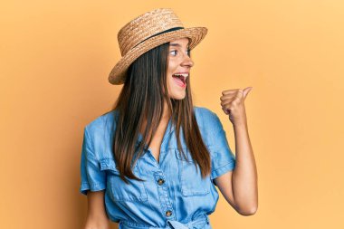 Yaz şapkası takan genç İspanyol kadın başparmağını yana kaldırarak mutlu bir şekilde gülümsüyor. 