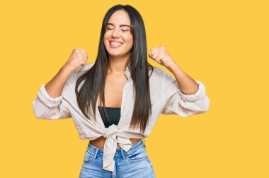 Gündelik giysiler giyen genç, güzel İspanyol kız. Başarı için heyecanlanan, kollarını kaldıran ve gözleri kapalı zaferi kutlayan kız. Kazanan konsept. 