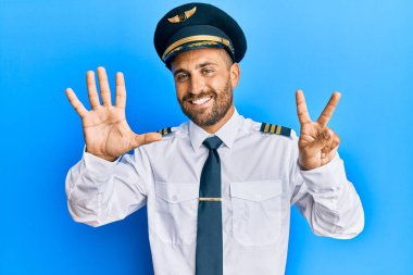 Sakallı, uçak pilotu üniforması giyen yakışıklı adam yedi numaralı parmaklarını gösterip gösterirken kendinden emin ve mutlu bir şekilde gülümsüyor.. 