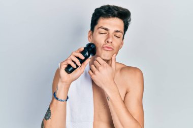 Elektrikli tıraş makinesiyle tıraş olan genç İspanyol bir adam kameraya bakıp öpüşürken sevimli ve seksi oluyor. aşk ifadesi. 