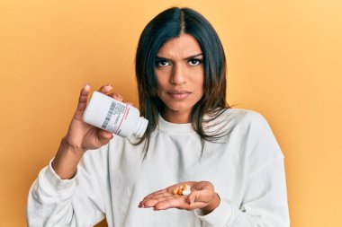 Genç Latin transseksüel kadın elinde haplar tutuyor şüpheci ve gergin, sorun yüzünden somurtuyor. negatif kişi. 