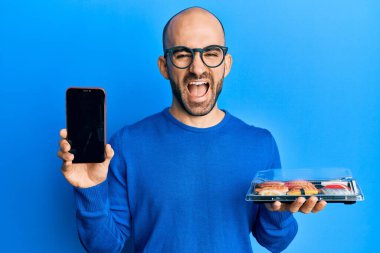 Genç İspanyol adam elinde yemek tutuyor akıllı telefon ekranını gösteriyor ve kahkahalarla gülüyor çünkü komik çılgın bir şaka.. 