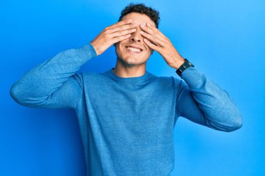 Sıradan bir kazak giyen İspanyol genç adam elleri gülücüklü ve komik bir şekilde gözlerini kapatıyor. kör kavram. 