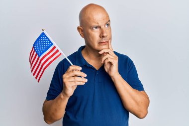 Orta yaşlı, kel bir adam Amerika Birleşik Devletleri bayrağını taşıyor. Ciddi bir yüz ifadesi var. Elleri çenesinde soru sormayı düşünüyor, kafa karıştırıcı fikirleri düşünüyor. 