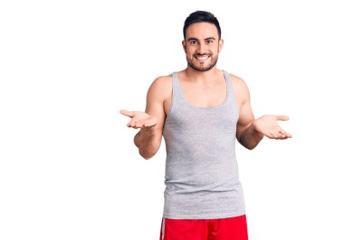 Mayo ve kolsuz tişört giyen genç yakışıklı adam, güler yüzlü ve kolları açık bir şekilde gülümsüyor. Hoş geldin, olumlu ve kendinden emin selamlar. 