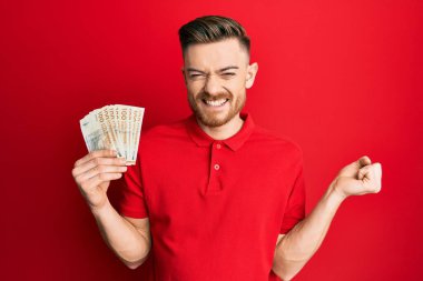 Genç kızıl saçlı adam elinde 100 Danimarka kronu ile gururla bağırıyor zaferi ve başarıyı kutluyor. 