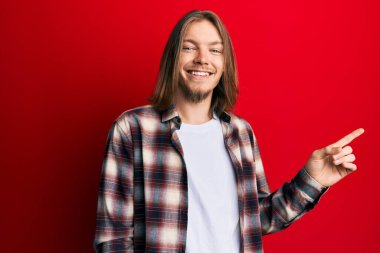 Uzun saçlı, yakışıklı, sıradan giyinmiş, gülümseyen, eli ve parmağı yanda olan beyaz bir adam. 