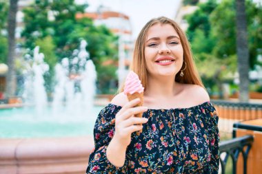 Genç kızıl saçlı kadın gülümsüyor. Şehrin caddesinde dondurma yiyor..