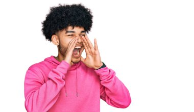 Afro saçlı, sıradan pembe kazak giyen, elleri ağzında kızgın bir şekilde bağıran Afro-Amerikalı genç bir adam. 