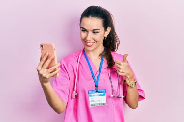 Genç esmer kadın, akıllı telefonuyla video görüşmesi yapıyor mutlu ve olumlu gülümsüyor, başparmağı mükemmel ve onay işareti yapıyor. 