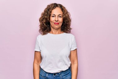 Yüzünde mutlu ve havalı bir gülümsemeyle izole edilmiş pembe arka planda duran sıradan tişörtler giyen orta yaşlı güzel bir kadın. Şanslı kişi..