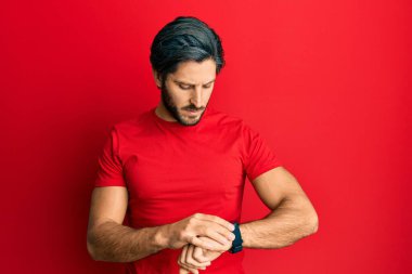 Gündelik kırmızı tişört giyen genç İspanyol adam kol saatini kontrol ediyor, rahat ve kendinden emin. 