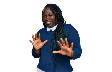 Saçları örgülü genç siyahi bir kadın iğrenç bir ifade takınıyor tiksinti tepkisi yüzünden tiksinmiş ve korkmuş bir ifade takınıyor. Eller havada. 