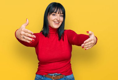 Gündelik giysiler giymiş genç İspanyol kadın kameraya bakıp sarılmak için kollarını açmış gülümsüyor. Mutluluğu kucaklayan neşeli bir ifade.. 