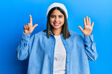 Şirin yün şapkalı genç Latin kadın yedi numaralı parmaklarıyla gülümseyerek mutlu ve kendinden emin görünüyor.. 