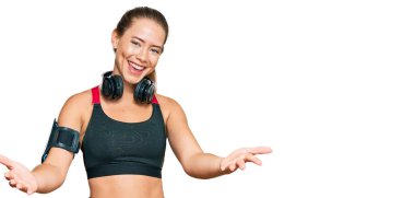 Güzel sarışın kadın spor kıyafetleri giyiyor ve kulaklık takıyor. Gülümsüyor. Yardım eli uzatıyor ve kabul ediyor.. 