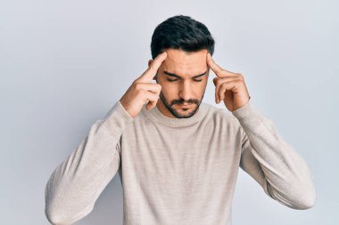 Latin asıllı genç bir adam elleri kafasında günlük kıyafetler giyiyor, stres yüzünden baş ağrısı çekiyor. migren ağrısı. 