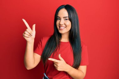 Gündelik kırmızı tişört giyen genç ve güzel İspanyol kız gülümseyip kameraya bakıyor ve iki eliyle ve parmaklarıyla kenarı işaret ediyor.. 