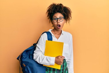 Afro saçlı, okul çantasıyla gezen, elinde kitap tutan, ağzı açık, korkmuş, şaşırmış ve şaşırmış güzel Afro-Amerikalı kadın. 