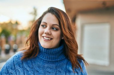 Genç İrlandalı artı cüsseli kız gülümseyerek şehirde mutlu mesut duruyor..