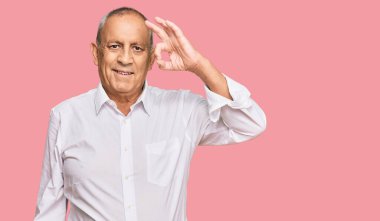 Zarif beyaz gömlek giyen yakışıklı bir adam gülümsüyor ve el ve parmaklarıyla 