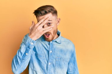 Genç kızıl saçlı bir adam, sıradan bir kot gömlek giyiyor. Şoka giriyor, yüzünü ve gözlerini eliyle kapatıyor, parmaklarından korkuyla bakıyor. 