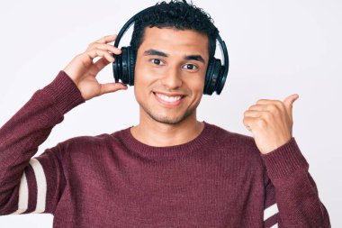 Genç, yakışıklı İspanyol adam müzik dinliyor kulaklık takıyor başparmağıyla yan tarafa bakıyor ve ağzı açık gülümsüyor. 