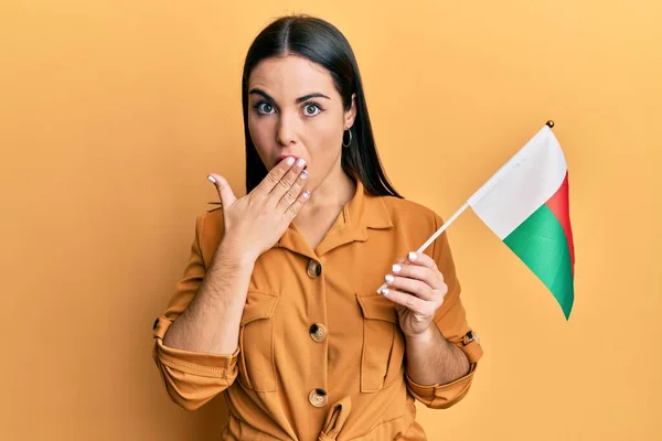 Jovem Morena Segurando Bandeira Madagascar Cobrindo Boca Com Mão Chocada — Fotografia de Stock