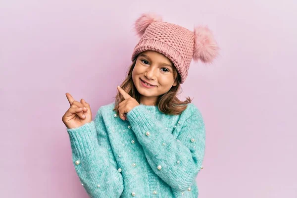 스웨터를 귀여운 모자를 아름다운 소녀가 웃으며 손가락으로 가리키고 카메라를 바라본다 — 스톡 사진