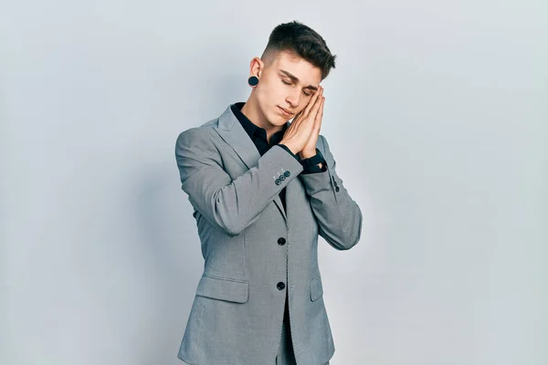 Young caucasian boy with ears dilation wearing business jacket sleeping tired dreaming and posing with hands together while smiling with closed eyes.